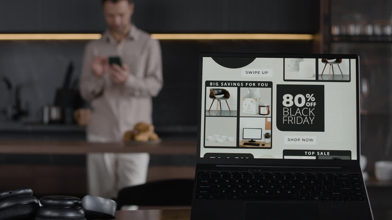 Man using phone with Black Friday sale on laptop in kitchen