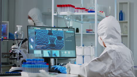 chemist in ppe suit typing on computer checking virus development