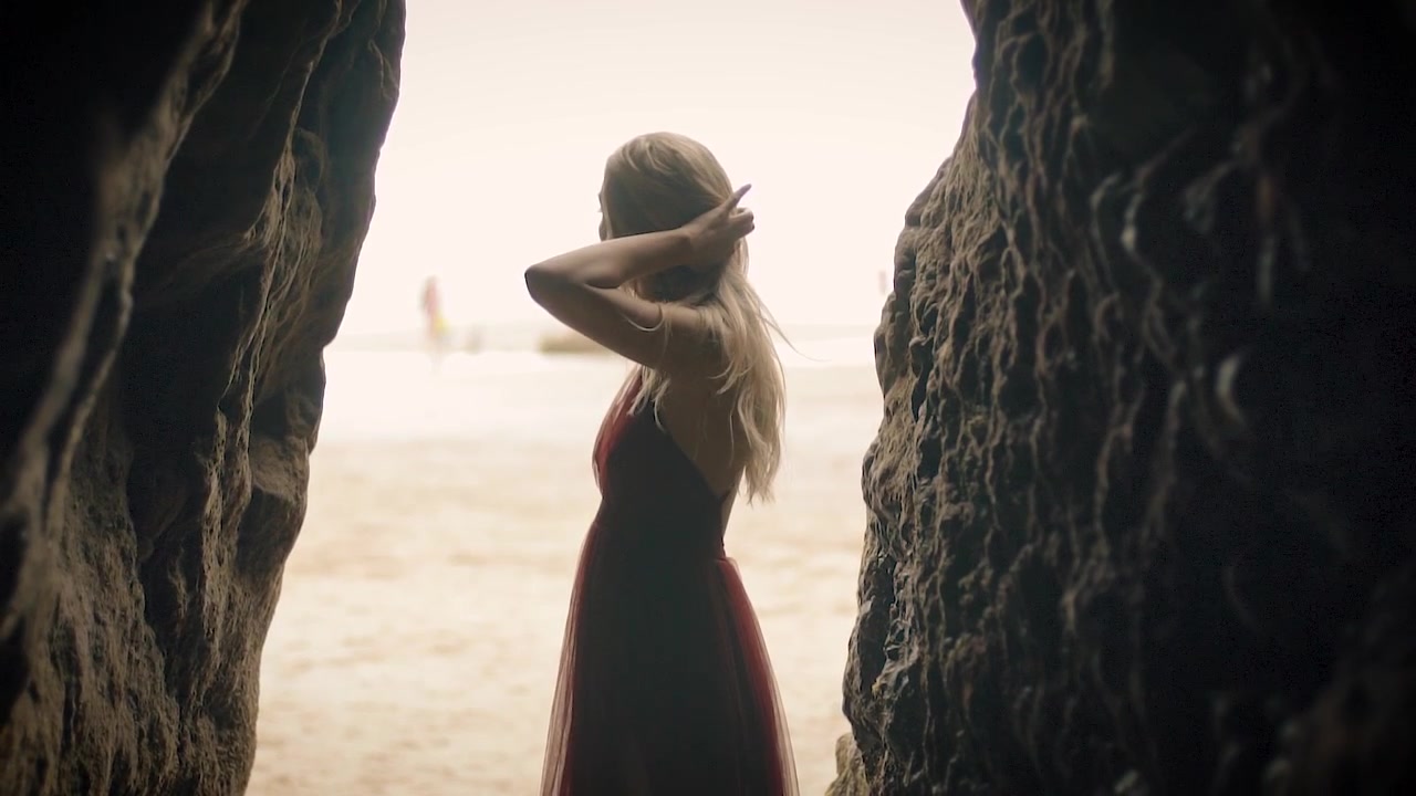 Modella in slow motion in posa sulla spiaggia con un vestito rosso.