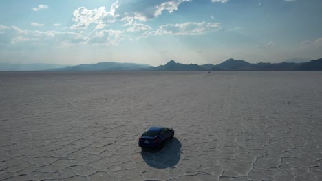 car riding across bonneville salt flats unique natural features with beam of sunlight rays shining through dramatic clouds and mountain touching horizon in background, utah, aerial tracking shot