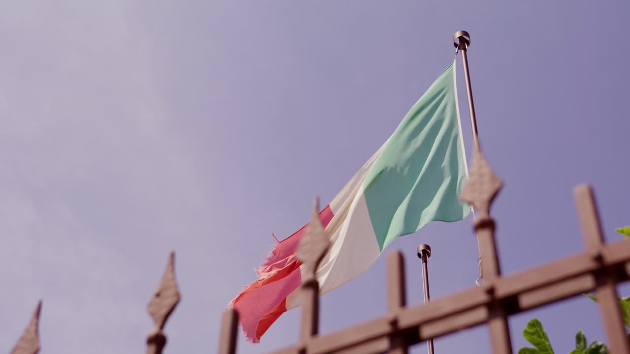 Italian flag waving in the breeze against a clear blue sky, angled view from below