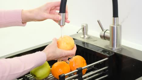 person washing fresh fruit in a modern kitchen sink