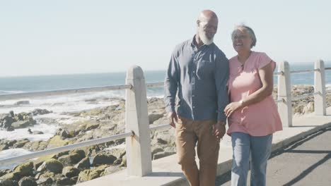 Happy-senior-african-american-couple-walking-along-promenade-by-the-sea,-slow-motion