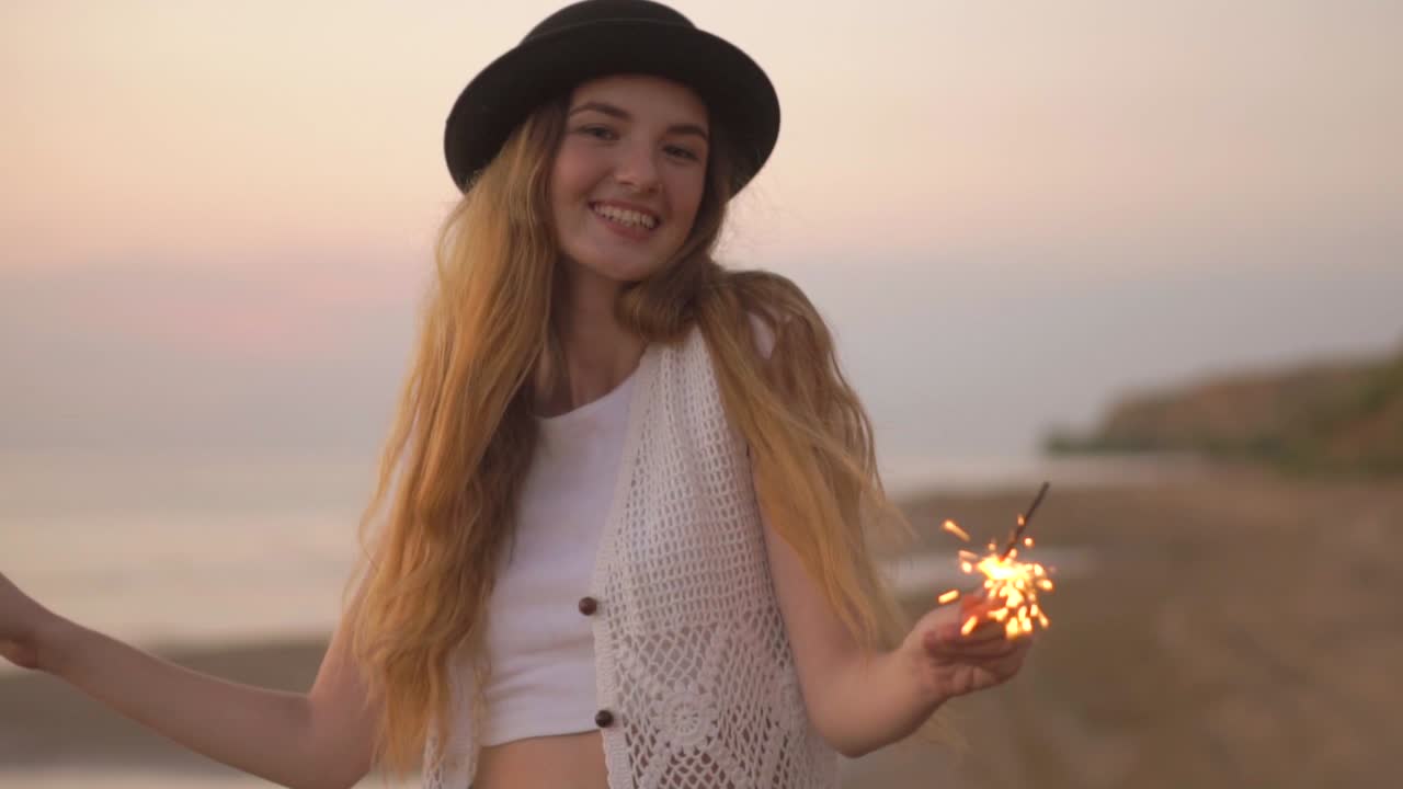 Young woman enjoying a sunset on the beach with sparklers