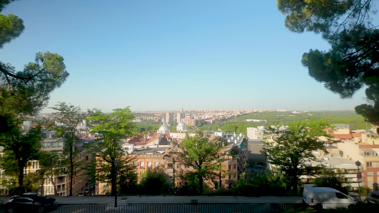 Un'ampia vista panoramica del paesaggio urbano di Madrid in Spagna, incorniciata da pini durante l'ora d'oro. Perfetto per documentari di viaggio e contenuti sullo stile di vita urbano.