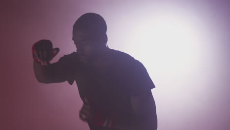 Dramatic-Backlit-Shot-Of-Male-Boxer-In-Gym-Wearing-Wraps-On-Hands-Training