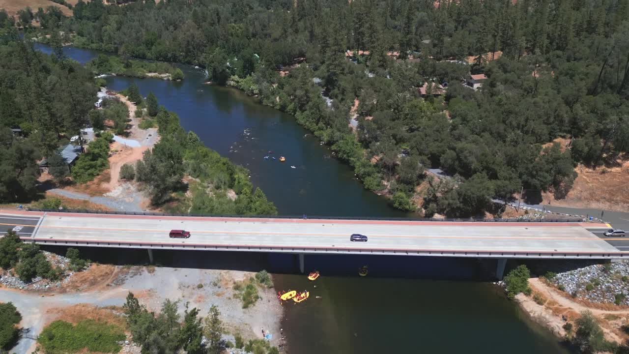 Aerial shot over a river in San Francisco with a bridge below, two cars crossing, and small boats drifting with the current on a clear, sunny day