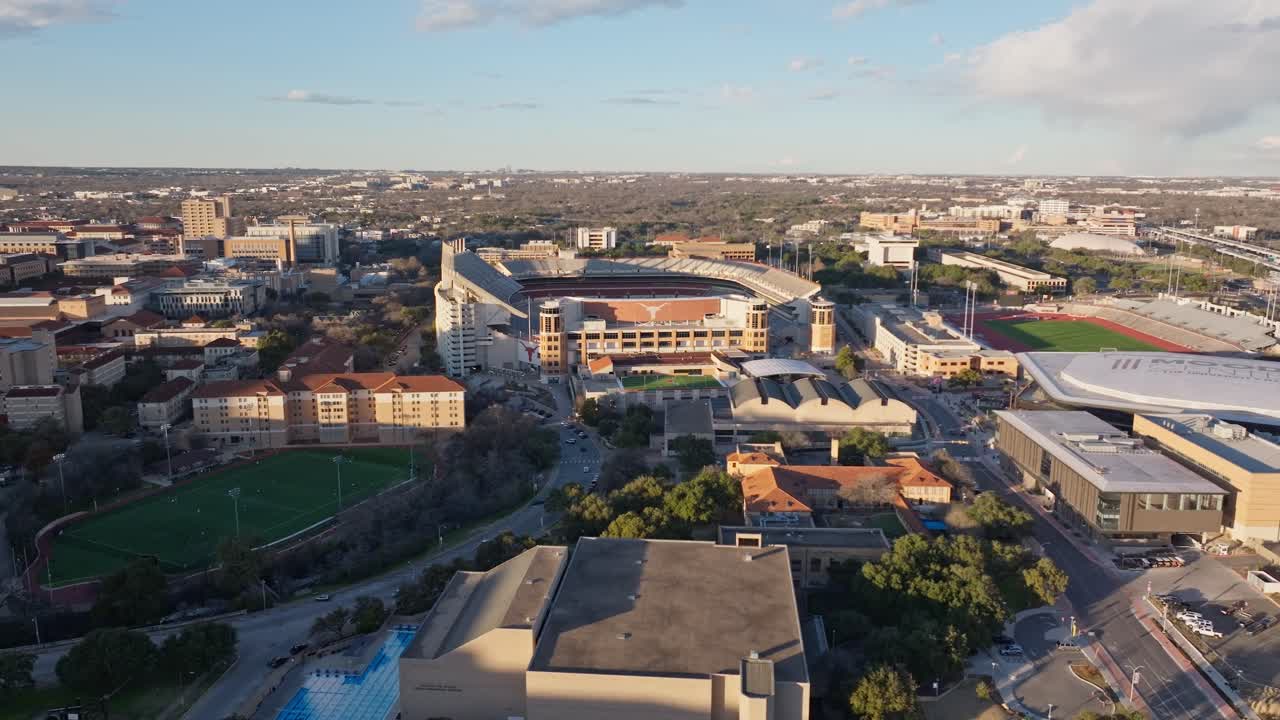 A wide drone shot at sunset panning left revealing and the empty Darrell K Royal Texas Memorial Stadium at the University of Texas (UT) in Austin and the surrounding videos
