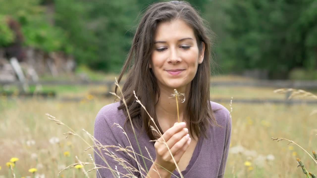 Wonderful slow motion shot of beautiful young girl blowing a dandelion in while relaxing in field of flowers on a gorgeous day