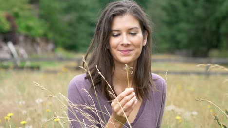 wonderful slow motion shot of beautiful young girl blowing a dandelion in while relaxing in field of flowers on a gorgeous day