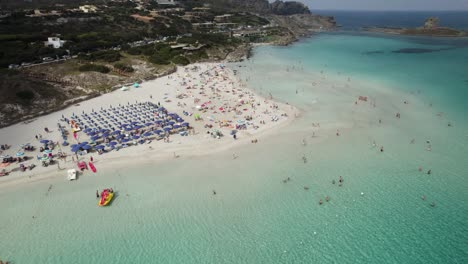 Toma-Aérea-Que-Establece-La-órbita-De-Una-De-Las-Playas-Más-Hermosas-De-La-Costa-Esmeralda-En-Cerdeña-Con-Gente-Tomando-El-Sol-Y-Nadando-En-Las-Aguas-Cristalinas