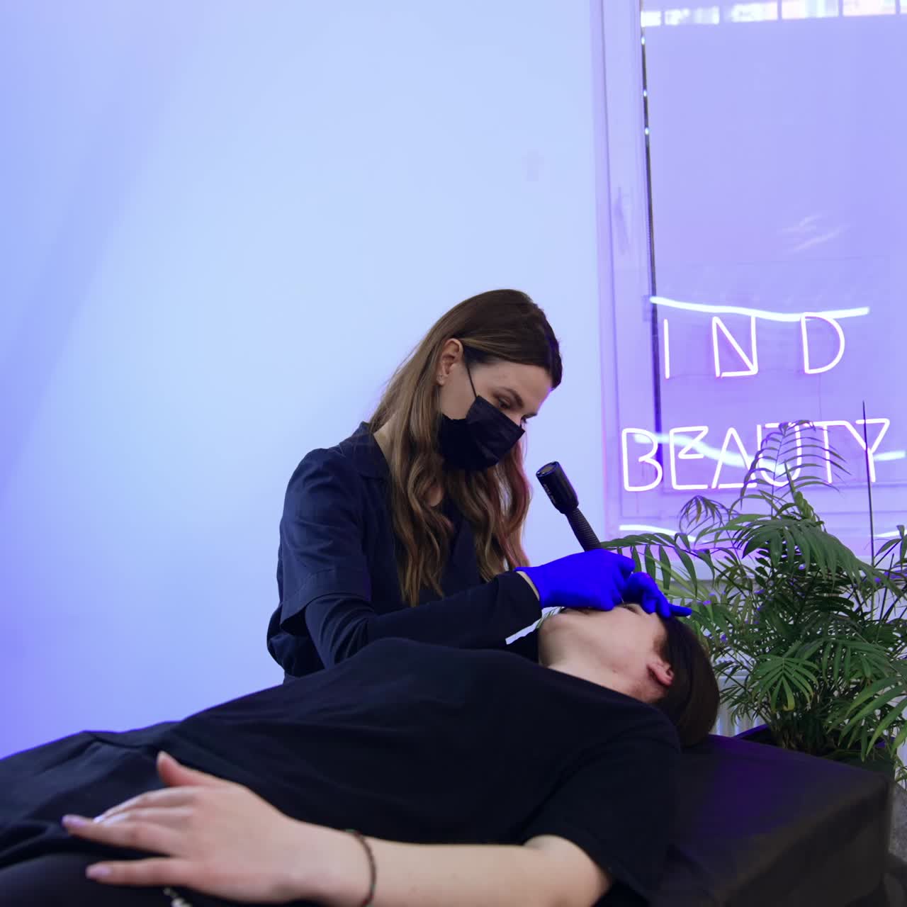 Caucasian brunette female lies on the couch in beauty salon. Beautician carrying out the procedure of permanent make up for eyebrows
