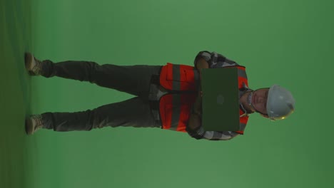 full body of asian male engineer with safety helmet working on a laptop while standing in the green screen background studio, during sunset or sunrise time
