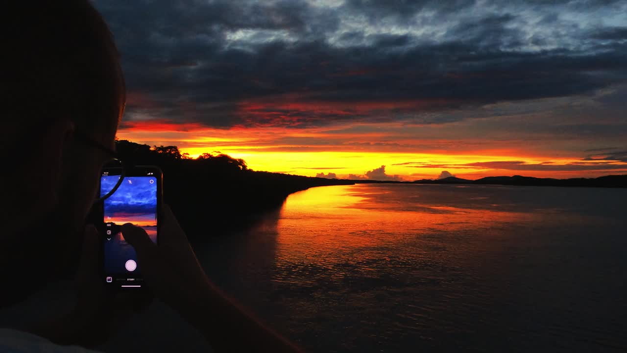 joven tomando una foto de la puesta de sol en costa rica con su aplicación de instagram en su teléfono