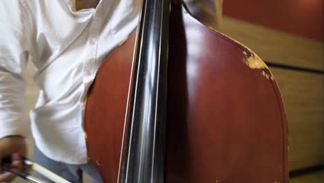 bottom up view of a mixed ethnicity roma gypsy male playing damaged weary antique instrument cello hitting notes strings natural romani talent hidden mysterious culture close up white shirt elder man