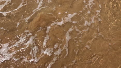 crystal clear transparent water splashes on shoreline sandy beach, handheld close up
