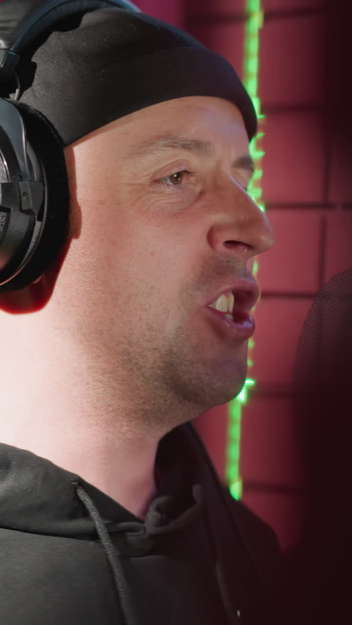 primer plano de un hombre vestido de negro, cantando apasionadamente en un micrófono en una sala de grabación a prueba de sonido. el cantante lleva auriculares y hace movimientos expresivos de las manos