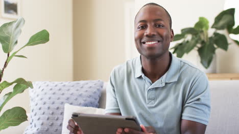 Un-Hombre-Afroamericano-Con-Una-Expresión-Alegre-Está-Usando-Una-Tableta-En-Casa-En-El-Sofá