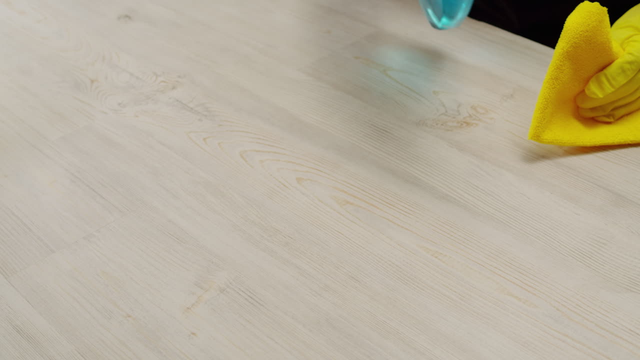 Hand in Yellow Glove Wiping Wooden Surface with Cleaning Spray