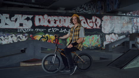 positive man having break after training on bmx bike at skate park graffiti.