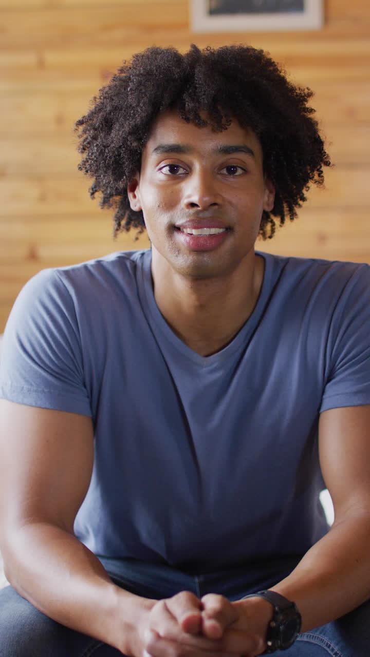 Vertical video of portrait of african american man looking at camera and smiling in log cabin