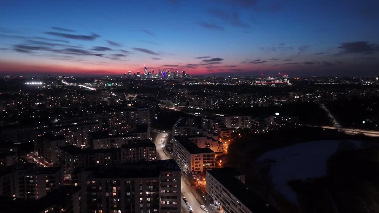 Warsaw - Poland - The city at night is full of apartment lights, with skyscrapers and city lights in the background. Panorama, drone flies forward