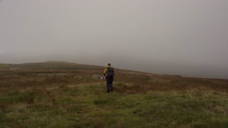 mann, der mit einem rucksack in richtung einer nebligen landschaft in schottland wandert