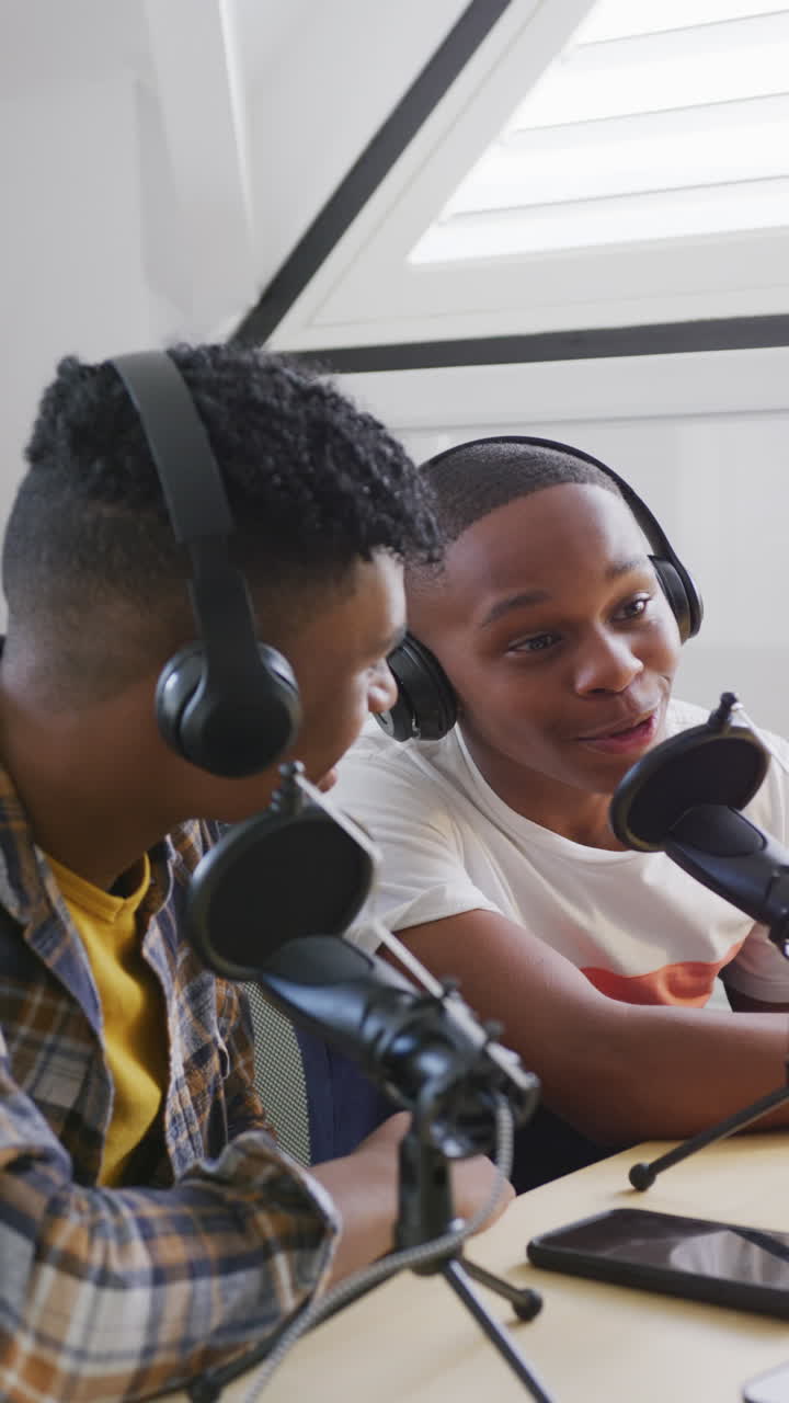 Vertical video of happy african american male teenage friends making vlog at home