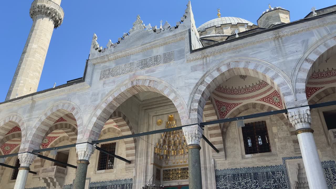 Historic mosque with domes and ornate minaret under bright midday sunlight, establishing push in