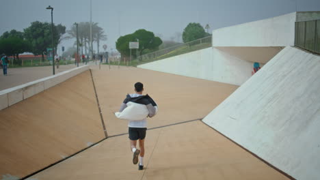 active guy running urban park rear view. athletic male training doing cardio