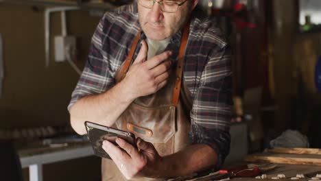 close up of focused caucasian male knife maker in workshop using tablet