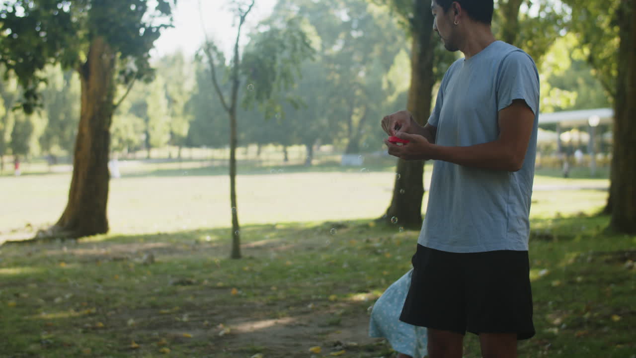 feliz chica asiática corriendo en el parque y padre soplando pompas de jabón