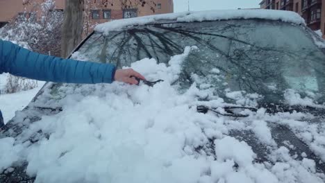 a woman´s arm scratching ice from a windshield