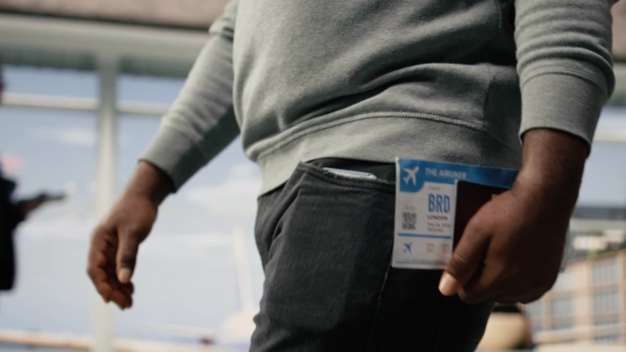 Close up of plane ticket and passport held by man walking in airport terminal