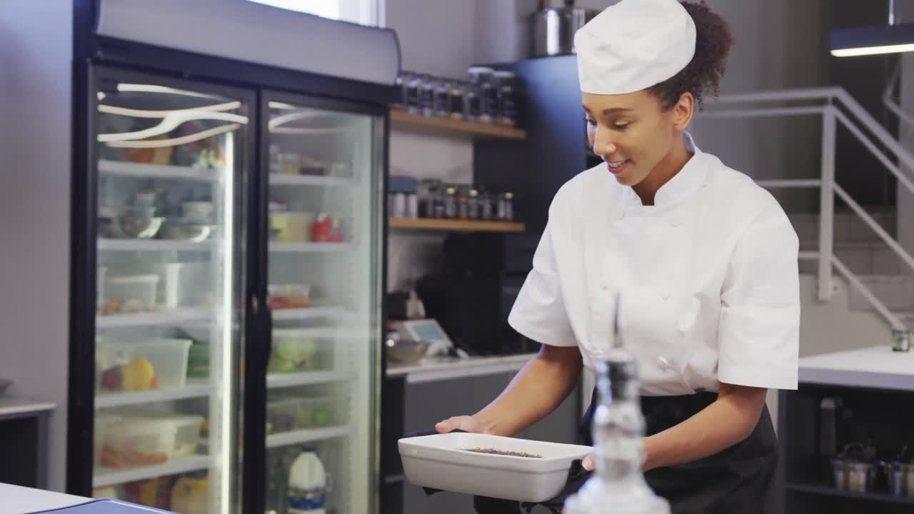 African American female chef wearing chefs whites in a restaurant kitchen,taking food out of an oven