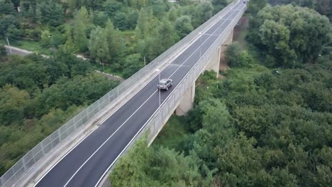 Drohnenaufnahme-Eines-Land-Rovers-Auf-Einer-Von-Bäumen-Umgebenen-Straße