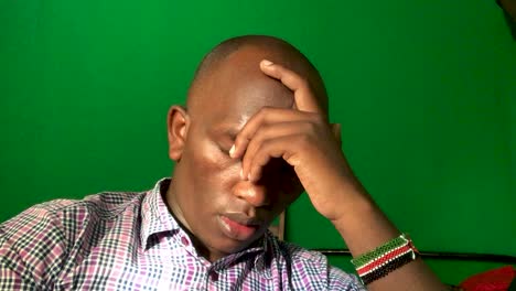 depressed and disturbed dark skinned man sitting at home in front of green screen. close up.