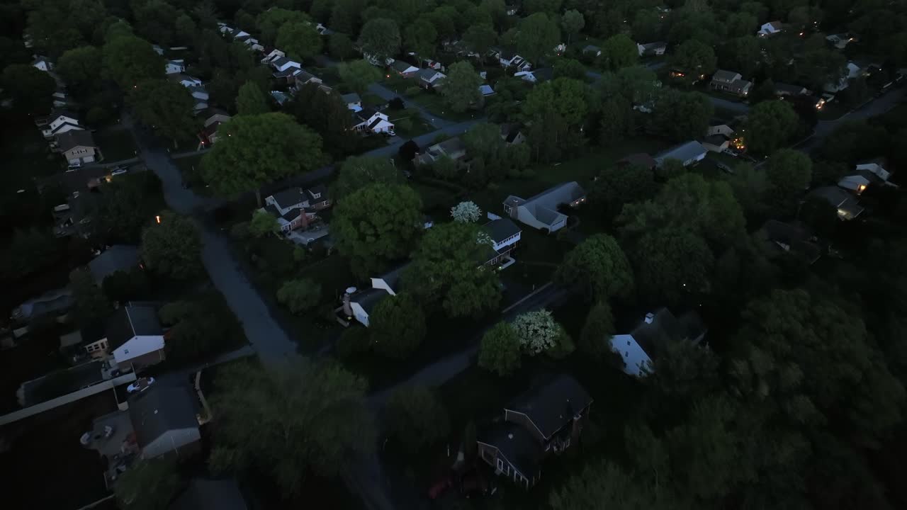 One Family Houses and garden during dark night in american city neighborhood. Green trees in spring season. Dusk scene. Sleeping families in family friendy housing area. Aerial top down flyover.