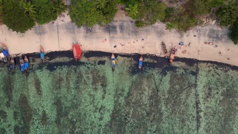 Bunte-Boote,-Die-An-Einem-Tropischen-Inselstrand-Vor-Anker-Liegen,-Mit-Touristen,-Die-Auf-Dem-Weißen-Sand-Spazieren