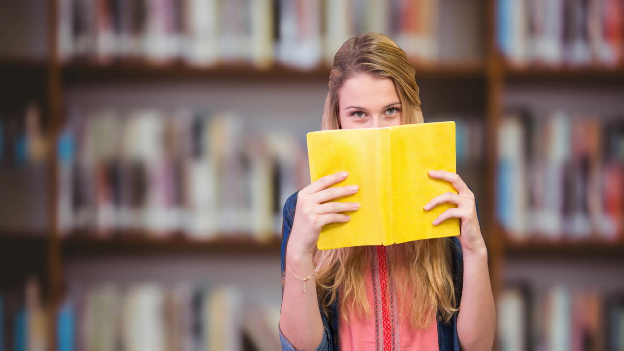 estudiante universitaria caucásica cubriendo su cara con un libro en la biblioteca