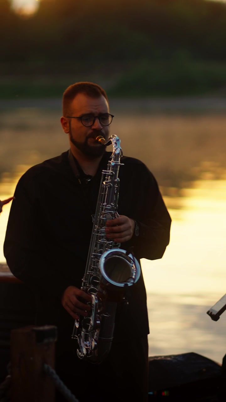 Musicista che suona il sassofono in riva al fiume al tramonto dorato