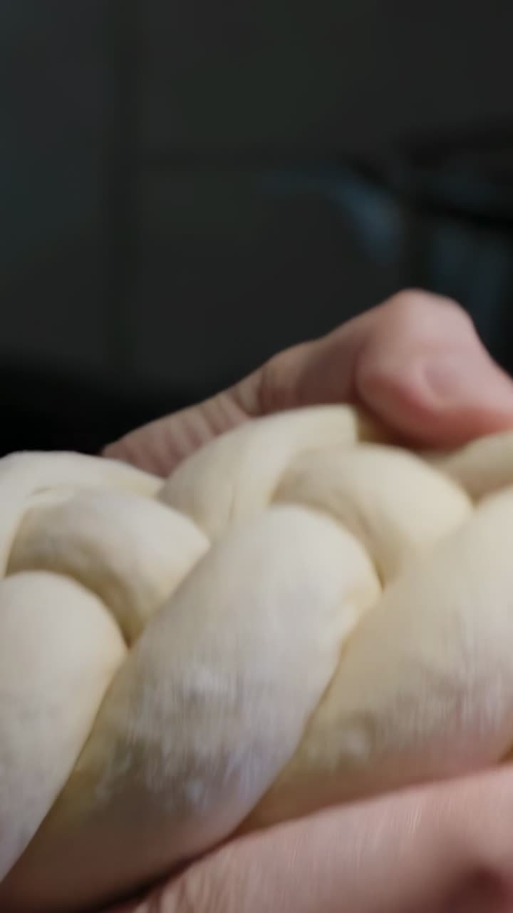 Vertical video: Hands entering frame, shaping braided loaf at home for uniformity in tan sleeves