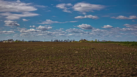 Toma-De-Tiempo-De-Nubes-Blancas-A-Lo-Largo-Del-Hermoso-Cielo-Sobre-El-Campo-De-Primavera-Arado-Al-Lado-De-Una-Carretera-Durante-El-Día