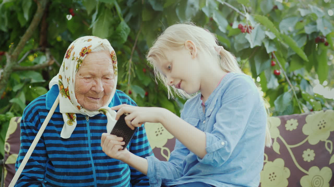 그 소녀는 세대 개념 4k 비디오의 스마트폰 친교에 할머니 사진을 보여줍니다