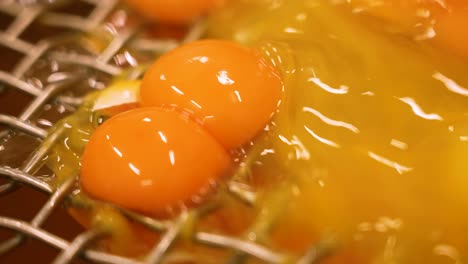 close up of many egg yolks falling through a small mesh or hole in a factory