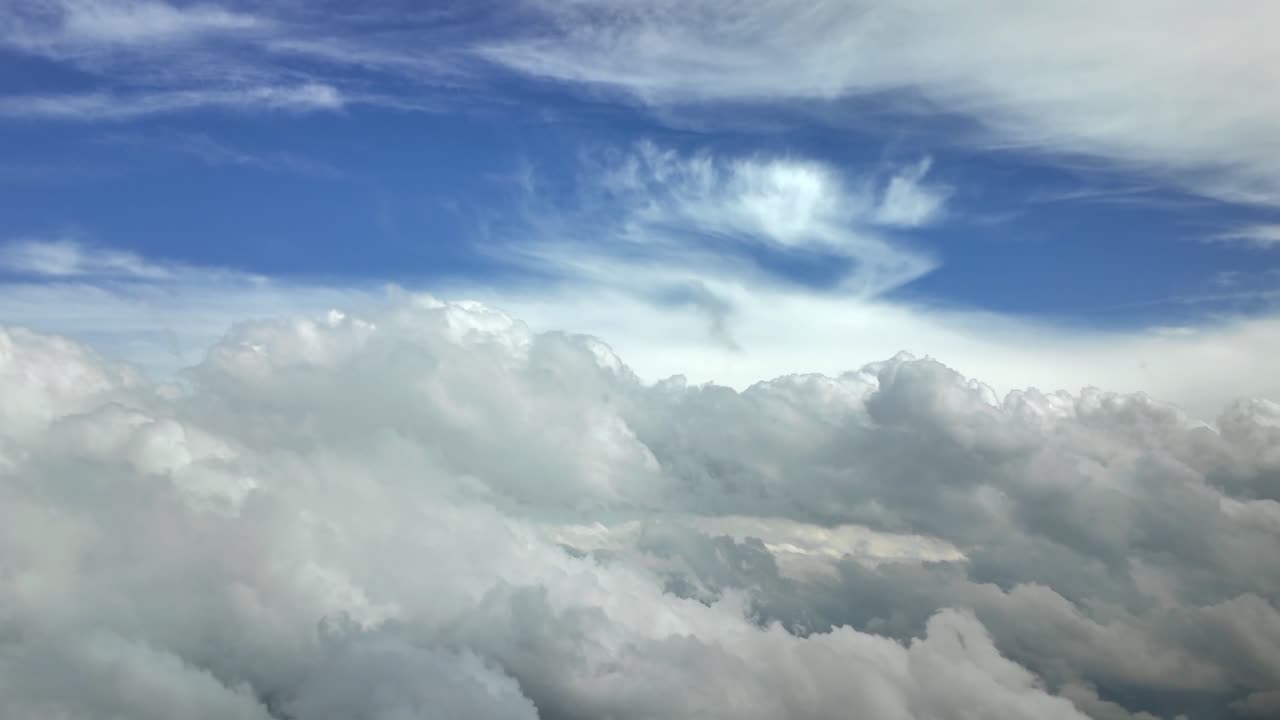 An aerial view taken from a jet cockpit while flying peacefully through a stormy sky full of white color cottony and stormy clouds under a blue sky. High-contrast, Ultra-realistic Shot. 4K