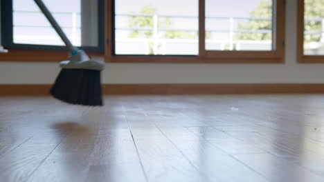 Low POV shot of broom sweeping hardwood floor of newly purchased apartment