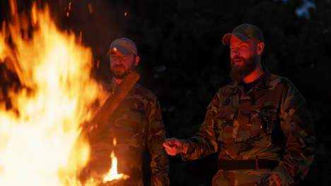 the military set up camp at night in the training areas, lit a campfire to warm up and frying sausages on sticks, the men were on duty, guarding the training ground, talking among themselves