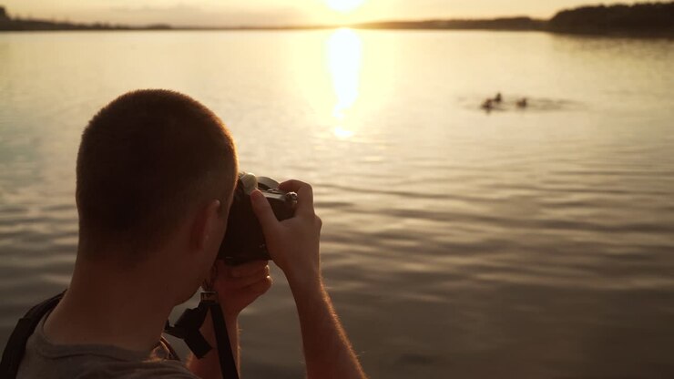 Un turista viene fotografato sulla spiaggia con persone che nuotano nel fiume al tramonto.