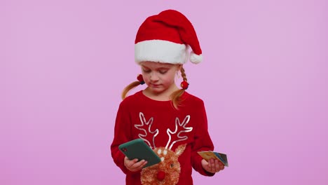 Girl-in-Christmas-sweater-using-credit-bank-card-smartphone-while-transferring-money-shopping-online